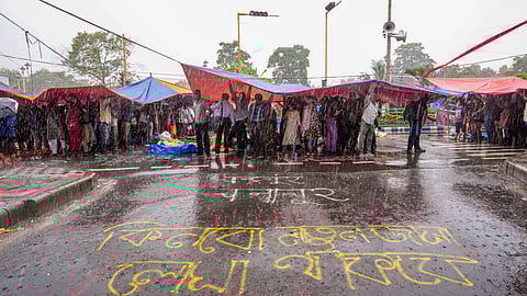 Agitators take cover during rains during sit-in demonstration against the RG Kar Hospital incident, outside Swasthya Bhavan in Kolkata, Friday, Sept. 13, 2024
