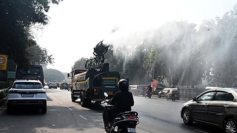 Commuters ride past an anti-smog gun spraying water to curb air pollution amid heavy smog conditions in New Delhi.